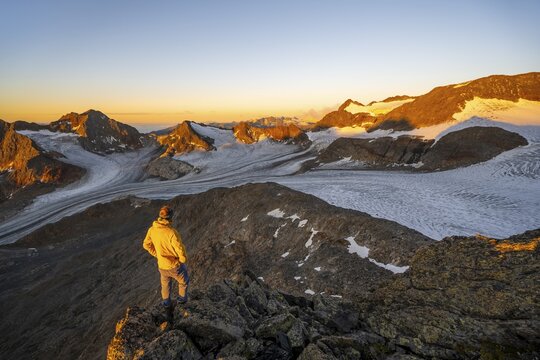 Mountaineer at the summit of the Becher, view of high mountain landscape with glacier &Uuml;beltalferner, alpenglow at sunrise, Stubai Alps, South Tyrol, Italy