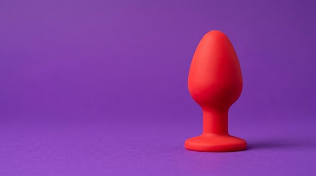Red silicone butt plug isolated on a vibrant purple background. Adult sex toy for pleasure and intimacy with copy space.