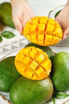 Fresh Diced Mango in Hands with Whole Green Mangoes