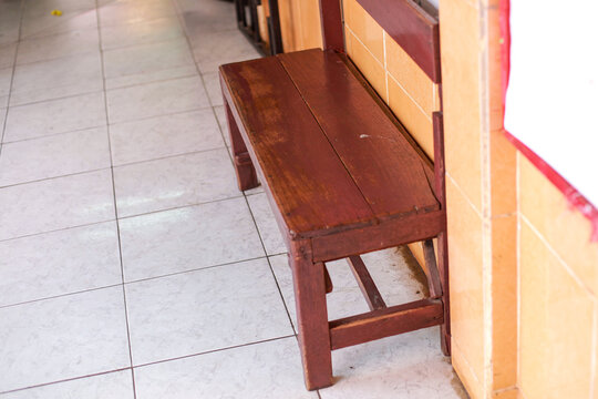 high-angle, perspective shot of an old, empty brown wooden bench placed against a yellow-tiled wall in a hallway
