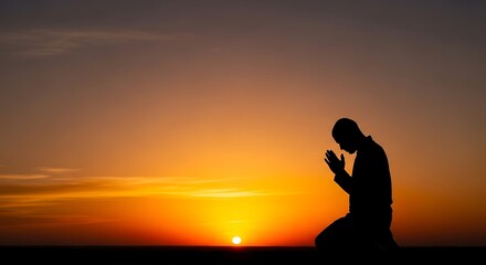 Fototapeta premium Silhouette of a man kneeling and praying to god during a sunset sunrise