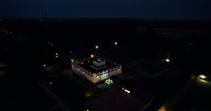 Aerial night drone shot of the floodlit Maya Devi Temple glowing in the darkness, surrounded by scattered lights in Lumbini, Nepal.