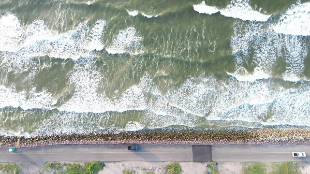 Wave struck seawall Surfside Beach frontage along Seashell Dr shows strong surf hitting rock lined barrier beside Gulf facing roadway. Sunlit water, bright foam highlights extend, Freeport, Texas