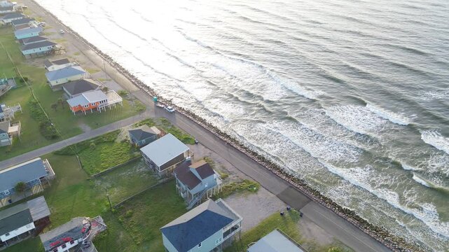 Coastal stilt homes Surfside Beach corridor along Seashell Dr presents elevated housing beside rock lined edge facing ocean view Gulf approach. Sunlit roofs, bright surf shimmer in Freeport, Texas