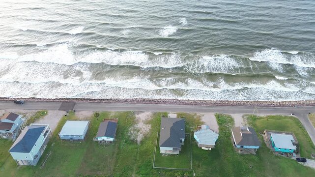 Coastal road frontage Surfside Beach frontage along Seashell Dr shows elevated homes beside shoreline barrier near Gulf facing corridor. Sunlit roofing, surf reflections extend in Freeport, Texas