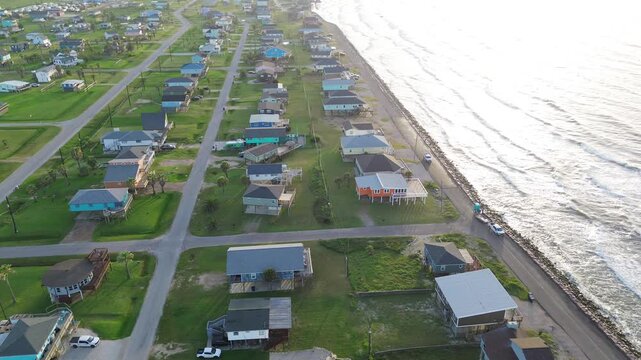 Shoreline residential rows ocean view Surfside Beach neighborhood near Seashell Dr displays raised homes arranged along Gulf facing roadway. Sunlit roofing, rolling surf glow frame Freeport, Texas