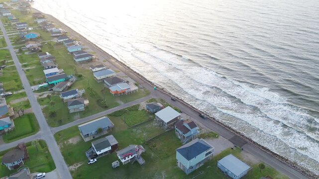 Shoreline barrier row Seashell Dr corridor sits beside stone lined waterfront near Surfside Beach edge with elevated homes facing open Gulf. Bright roofing, water contrasts in Freeport, Texas