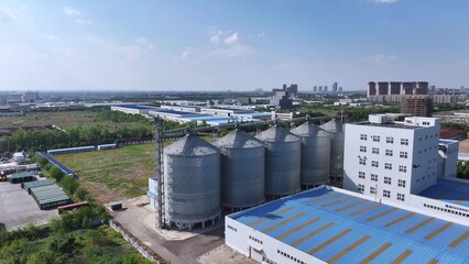 Industrial complex featuring large metal grain silos and factory buildings under clear blue sky © zhu difeng