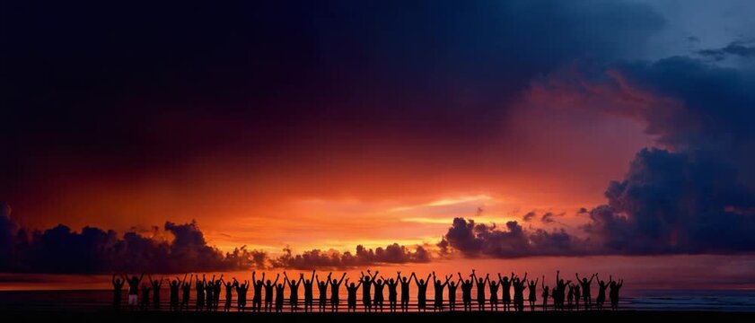 Unity at Dusk: A large group of people stand in silhouette with arms raised, facing a breathtaking sunset over the ocean, embodying collective hope and shared experience.