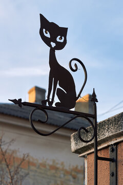 Decorative metal cat silhouette sign mounted outdoors against soft sky background