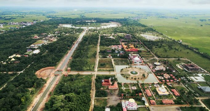 High aerial drone panorama of the entire Lumbini monastic zone with its central canal, temples, ponds and gardens stretching across the plains of Nepal.