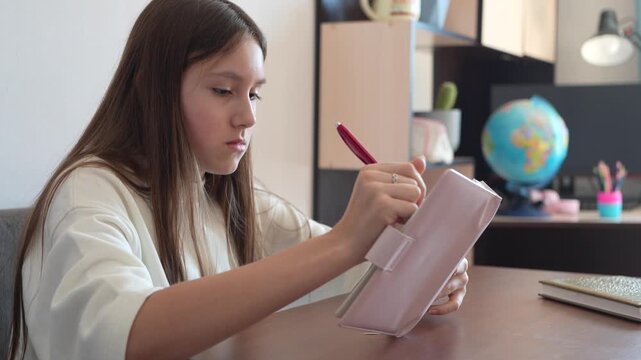 Young girl writing thoughts in her personal pink diary. Focused teenager making notes in notebook at desk, peaceful moment of self-reflection and journaling.