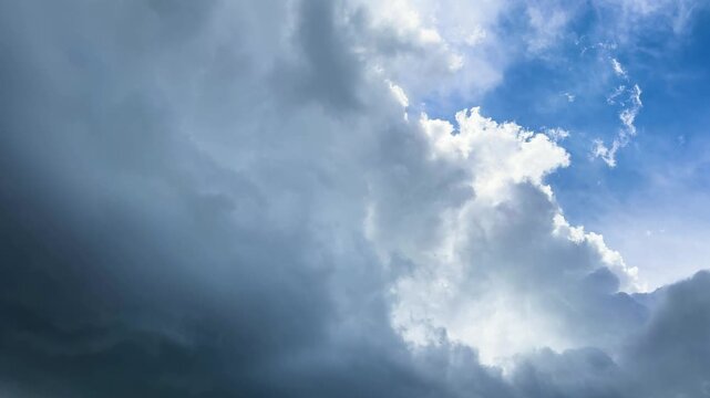 Dramatic thunderclouds against blue sky and sunlight, gloomy weather background with dark rain clouds