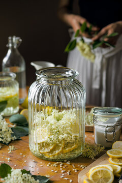 Preparation of elderberry flower syrup, ingredients and accessories visible on the table,  soft light with deep shadows.