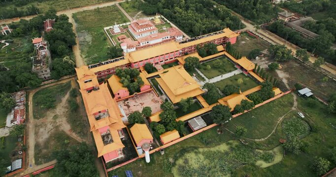 Aerial drone view of a large golden-roofed Buddhist monastery complex with courtyards and gardens surrounded by greenery in Lumbini, Nepal.