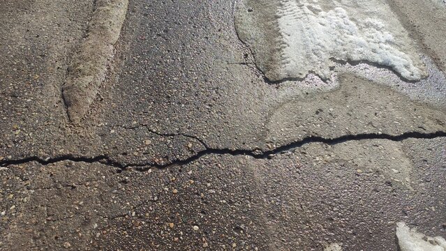 Fissured Asphalt Pavement showing a long crack across the gray road surface. Suitable for infrastructure damage reports, driving hazard warnings, and grunge backgrounds.
