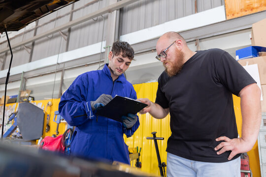 Mechanic checks car engine while customer looks on inside auto repair shop