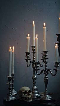 Elegant silver candelabras with burning candles and skull in dim light