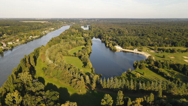 Aerial view of the Seine river flowing past a lush forested island and green parklands in Chartrettes, Ile-de-France, France.