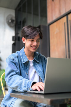 Young Asian non-binary man smiling using laptop at cafe portrait