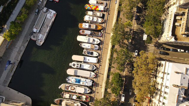 Aerial view of boats docked along the canal in Paris, with urban streets and trees lining the waterfront in Paris, Ile-de-France, France.