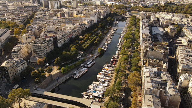Aerial view of Canal Saint-Martin lined with historic apartment buildings, tree-lined banks, and moored boats in Paris, Ile-de-France, France.