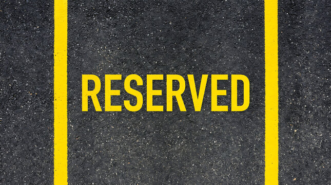 Yellow word RESERVED on asphalt surface parking spot markings for private vehicle space