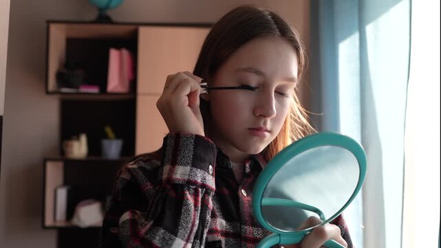 Girl applying mascara to eyelashes using brush while looking in mirror.