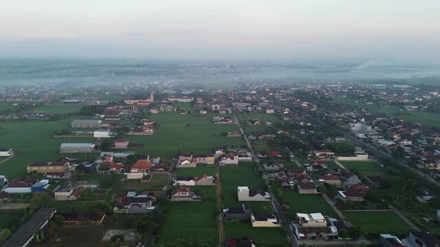Drone aerial view of Karanganyar, a small town in Central Java, Indonesia, during a peaceful morning with warm sunrise light illuminating the urban landscape and residential neighborhoods.