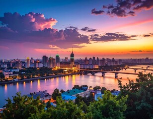 Fototapeta premium A scenic cityscape view, with buildings illuminated, a river, bridges and trees under a vibrant sunset sky