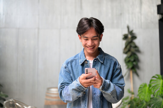 Young Asian non-binary man smiling using phone by corrugated wall wide