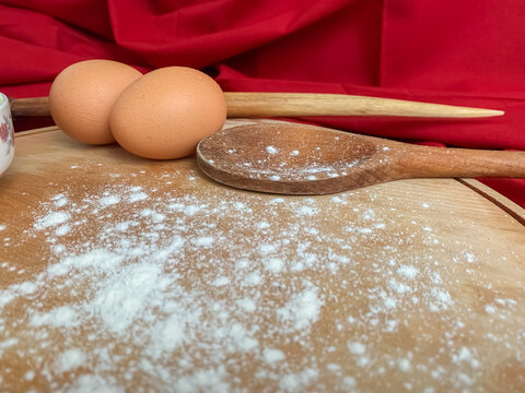 Rustic kitchen scene with fresh eggs and a wooden spoon on a floured board.