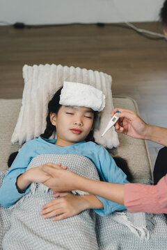 A concerned mother taking a temperature reading for her sick daughter lying in bed