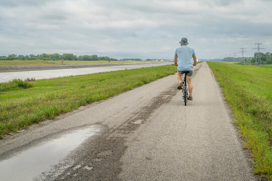 athletic man is riding a folding bike - biking on a levee trail along Chain of Rocks Canal near Granite City in Illinois