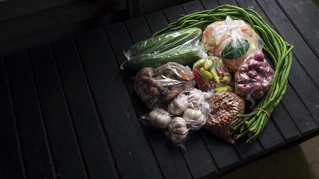 Top down view of various raw asian cooking ingredients and fresh vegetables wrapped in plastic bags arranged on a dark wooden slatted table