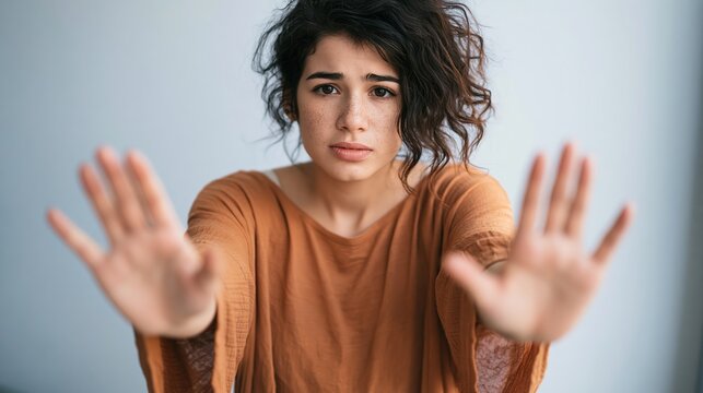 Young woman with freckles holds up her hands in a stop gesture, looking concerned