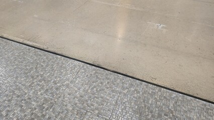 Fototapeta premium Contrast texture between polished concrete floor and grey mosaic tiles. Top view of floor material transition showing a split between smooth cement flooring and patterned tiles.