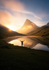 Fototapeta premium Hiker with Raised Arms Celebrating Success at Sunrise by a Calm Mountain Lake Reflection