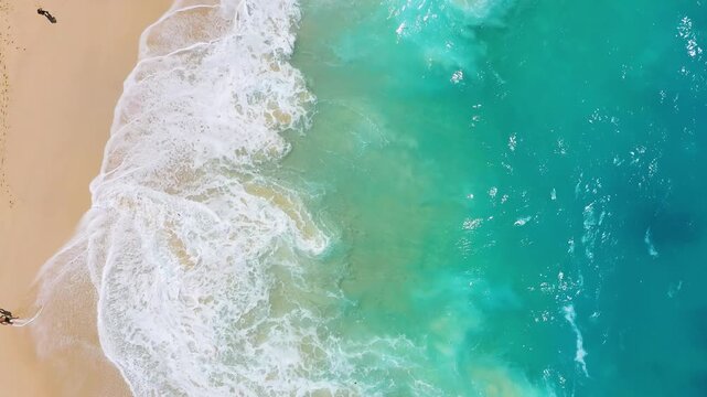 Aerial top down view of big ocean waves crashing on a sandy beach. Nature background with sea surf foam for summer vacation and travel concepts.