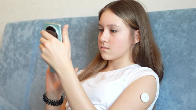 teenager girl checks his blood sugar level using a smartphone and a continuous glucose monitoring system.