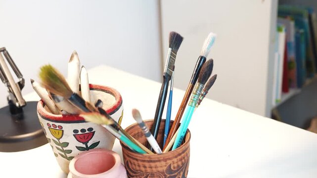Artist putting paintbrushes into a clay cup on a studio table