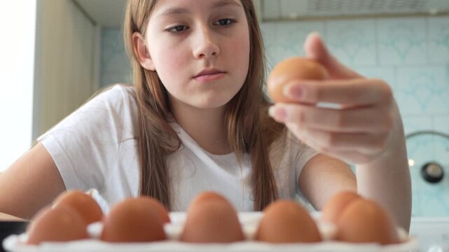 Teenage girl in the kitchen choosing and checking a brown egg from a carton while preparing to cook. Healthy cooking and daily routine concept.