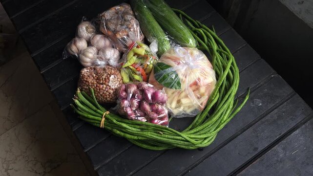 Top-down perspective of fresh vegetables and cooking ingredients packaged in plastic bags on a dark wooden table
