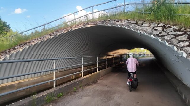 Middle aged woman riding electric bicycle through bike underpass on cycling route
