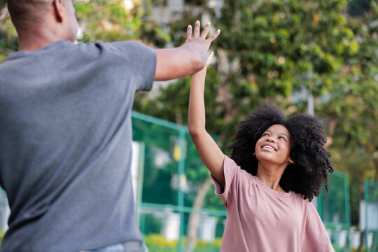 Father and daughter high-five in a park, smiling.