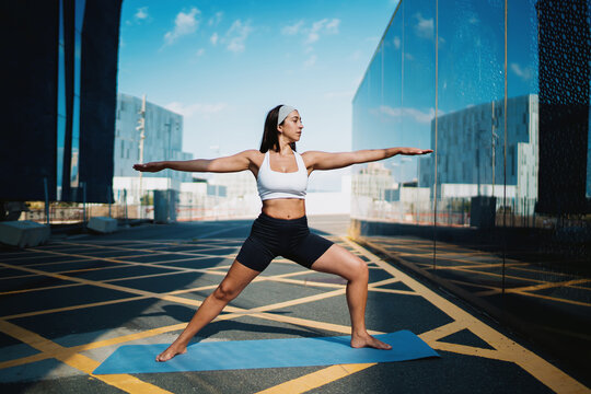 Confident woman holding warrior pose, centered on mat, arms fully extended, aligned with city symmetry, showing mental strength, body tone, and flow of mindful digital movement.