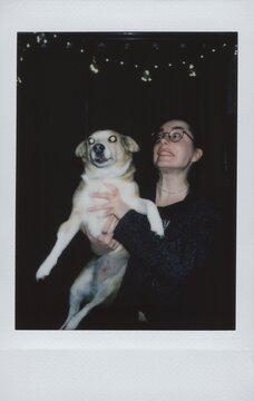 A funny woman in glasses holds a dog with eyes glowing from a flash