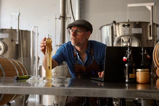Brew master tests liquid in a brewery while wearing a cap and apron