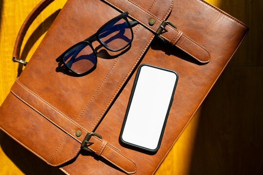 Brown bag, glasses, and phone on wooden table