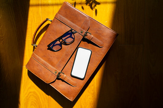 Brown bag, glasses, and smartphone on a table